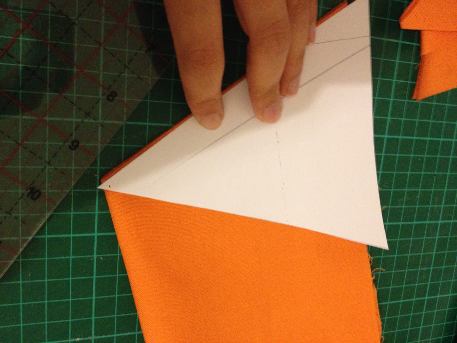 A person demonstrating a Halloween bunting tutorial by cutting an orange paper on a cutting board.