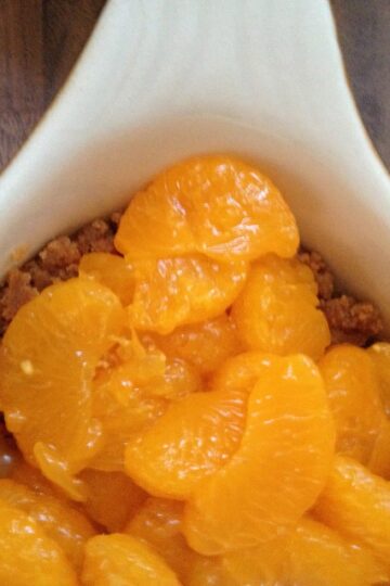 A white bowl with mandarins in it.