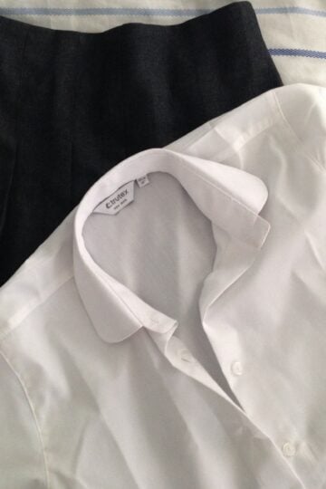 Two shirts, one white and one black, laid out on a bed for a Trutex school uniform review.