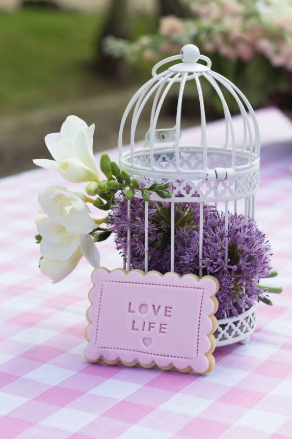 an iced biscuit in front of a white birdcage filled with white and purple flowers