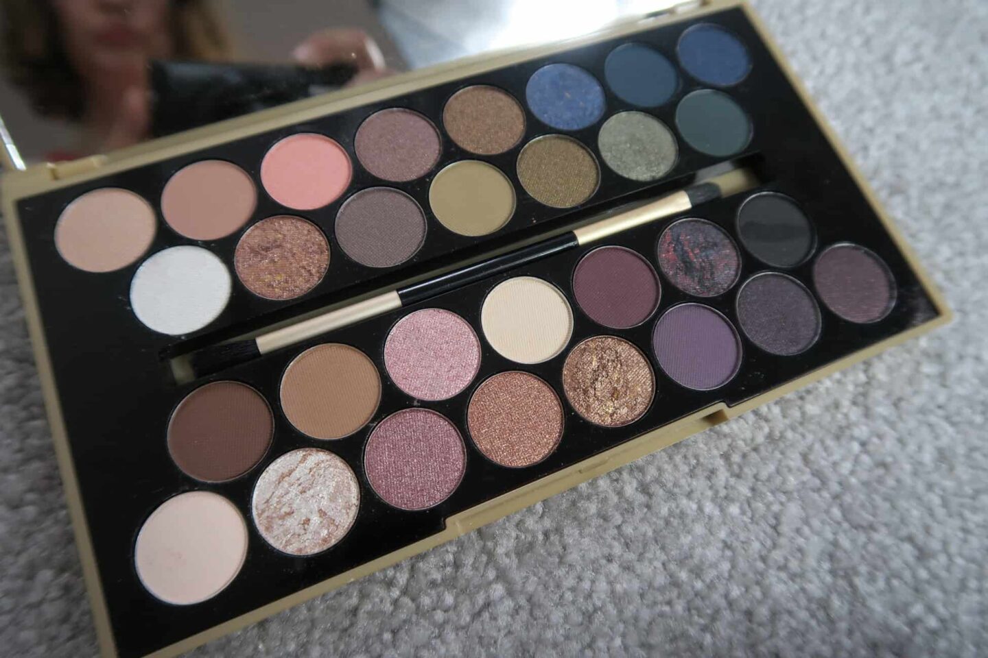 A make-up palette in a box on a carpet.