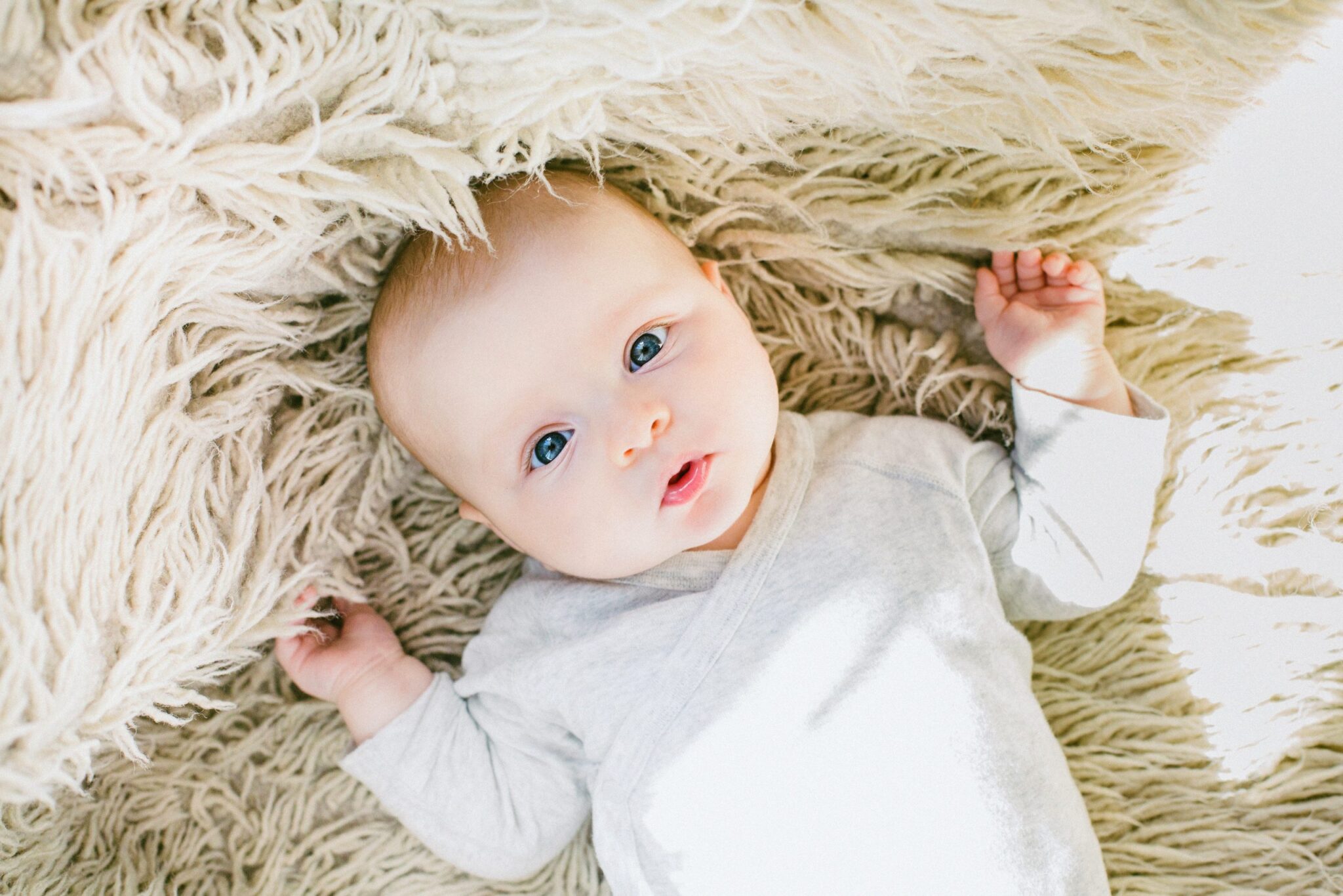 baby in a white onesie on a fluffy cream rug