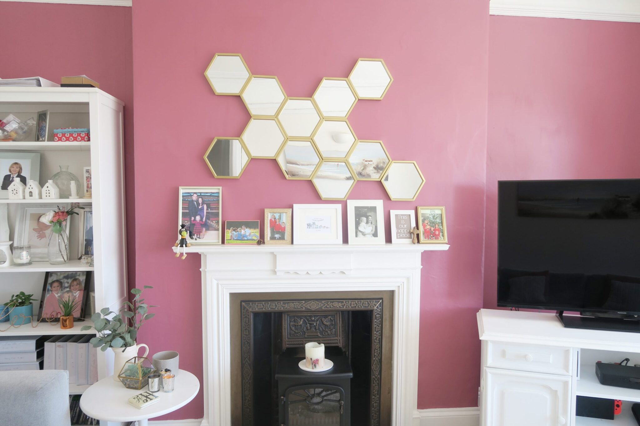 gold hexagonal mirror above a fireplace on a pink wall