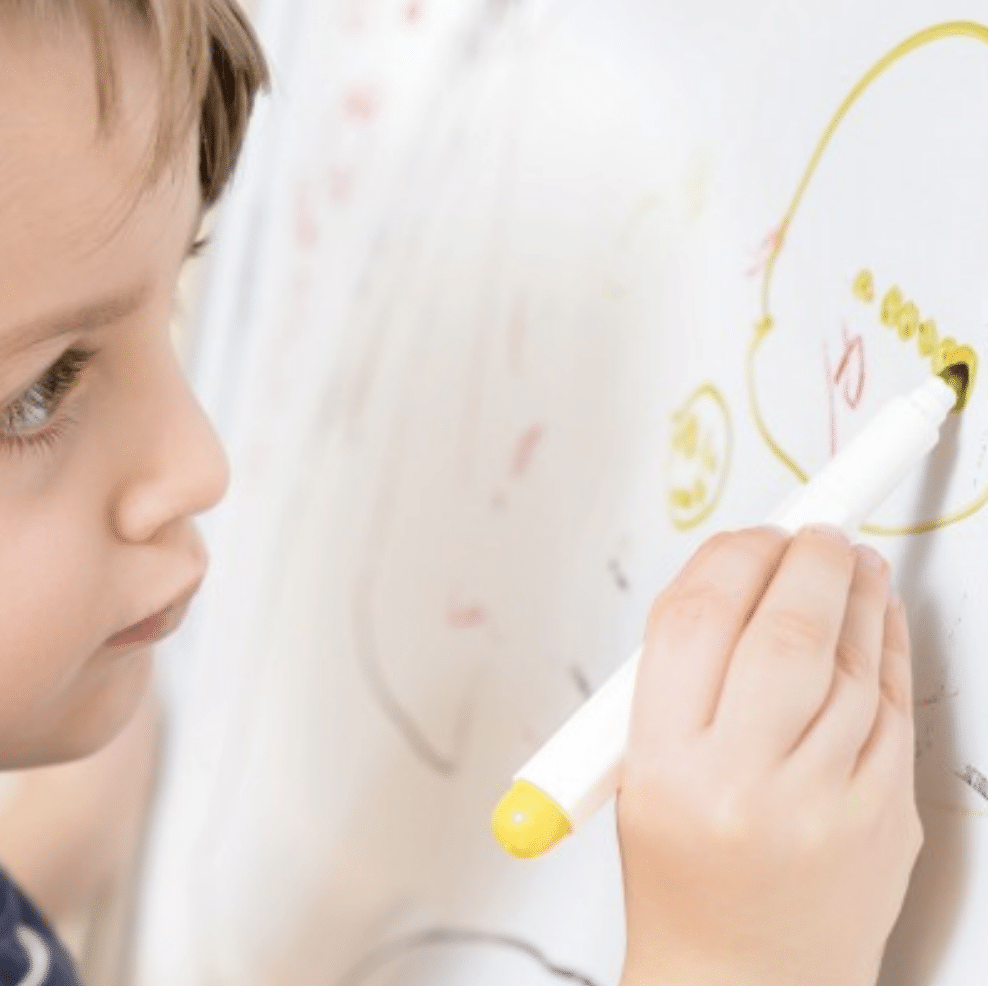 a child drawing on a dry erase board with a yellow whiteboard pen