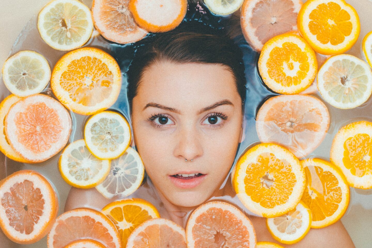 A lady's face looking out from a bath filled with orange slices
