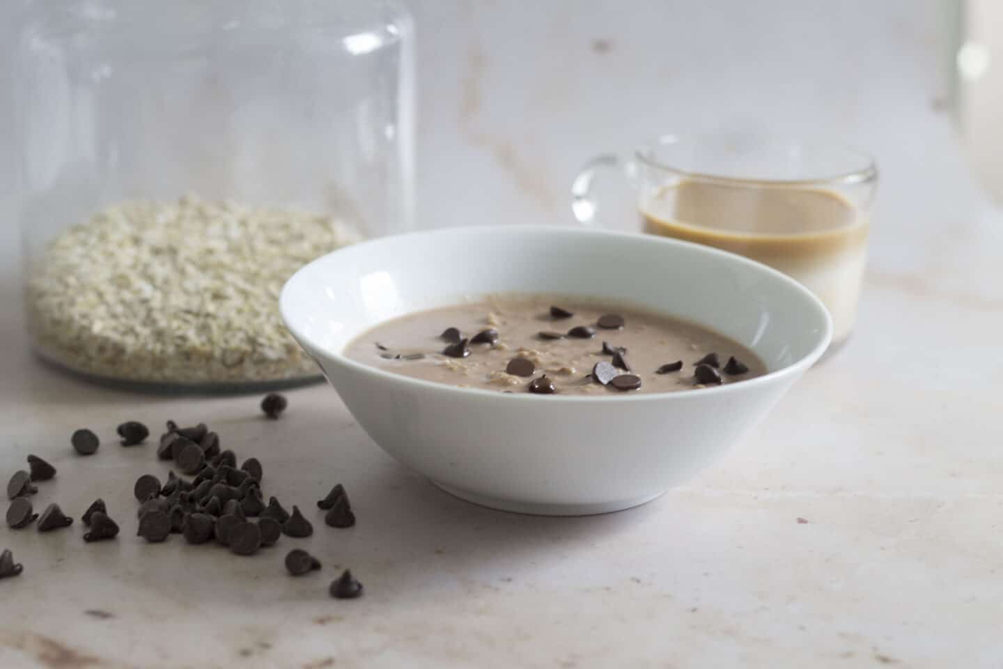 a bowl of chocolate porridge with a jar of oats and a coffee in the background
