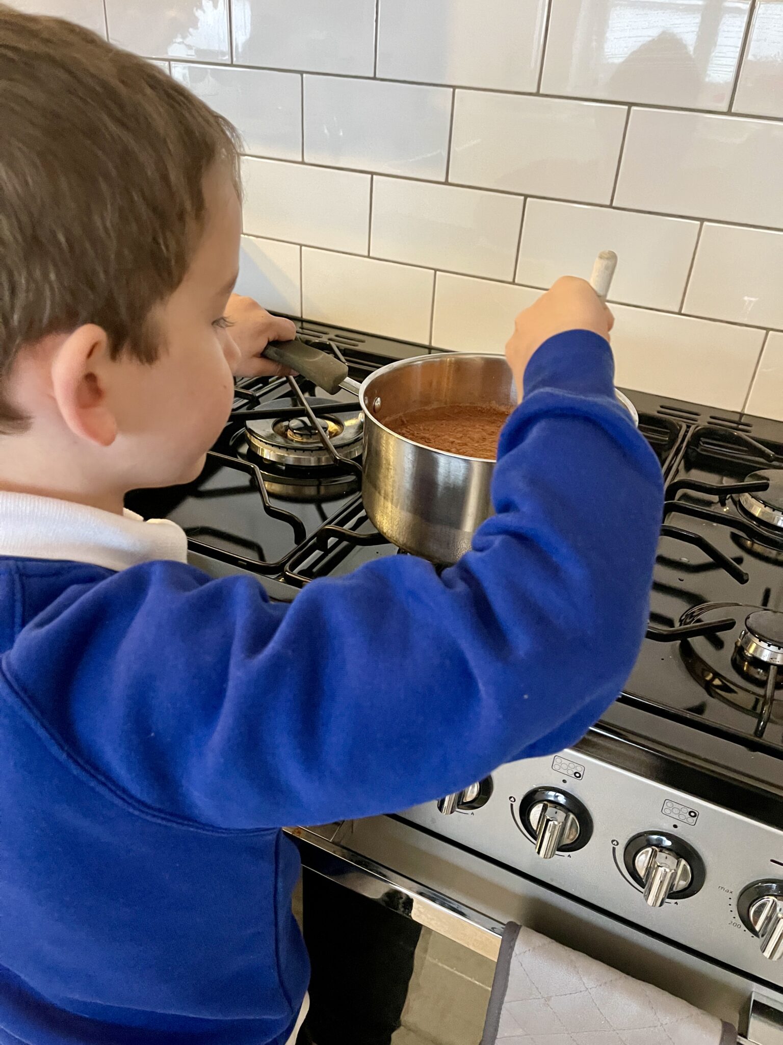 7 year old boy stirring chocolate porridge on the hob