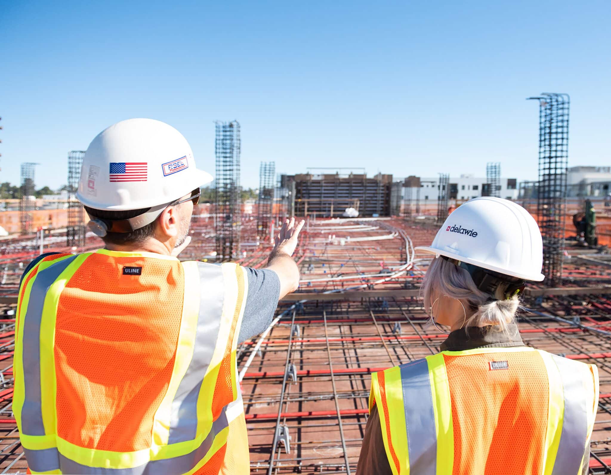 two construction workers wearing high visibility vests and hard top hats overlooking a huge building project