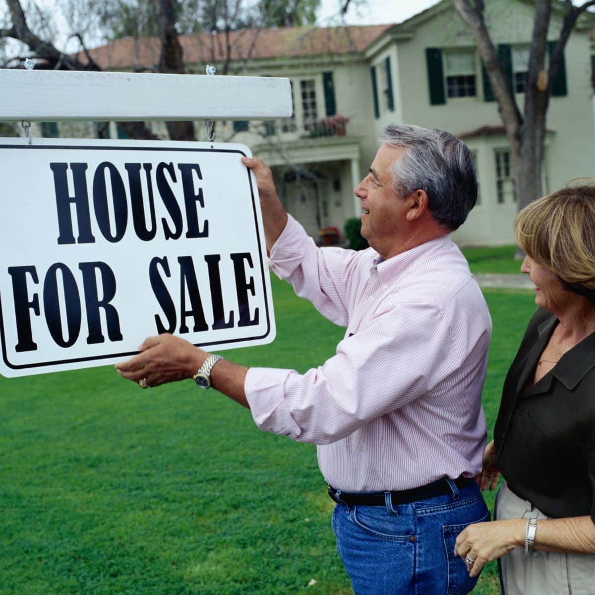 A man and woman standing next to a "Prepare Home for Sale" sign.