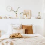 A tidy and well-decorated bedroom renovation with a neutral color palette showcasing a made bed with pillows and a textured throw, accompanied by a shelf with books and minimalistic decor items, and a chocolate