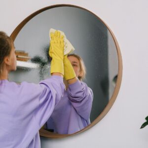 a woman wearing yellow rubber gloves cleaning a mirror.