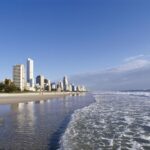 A city skyline adjacent to a sandy beach with gentle waves lapping at the shore in Far North Queensland.