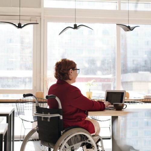 A woman in a wheelchair utilizing a laptop for independent aging in an office setting.