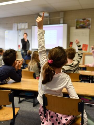 A group of children sitting at desks in a classroom, constantly annoying their parents.