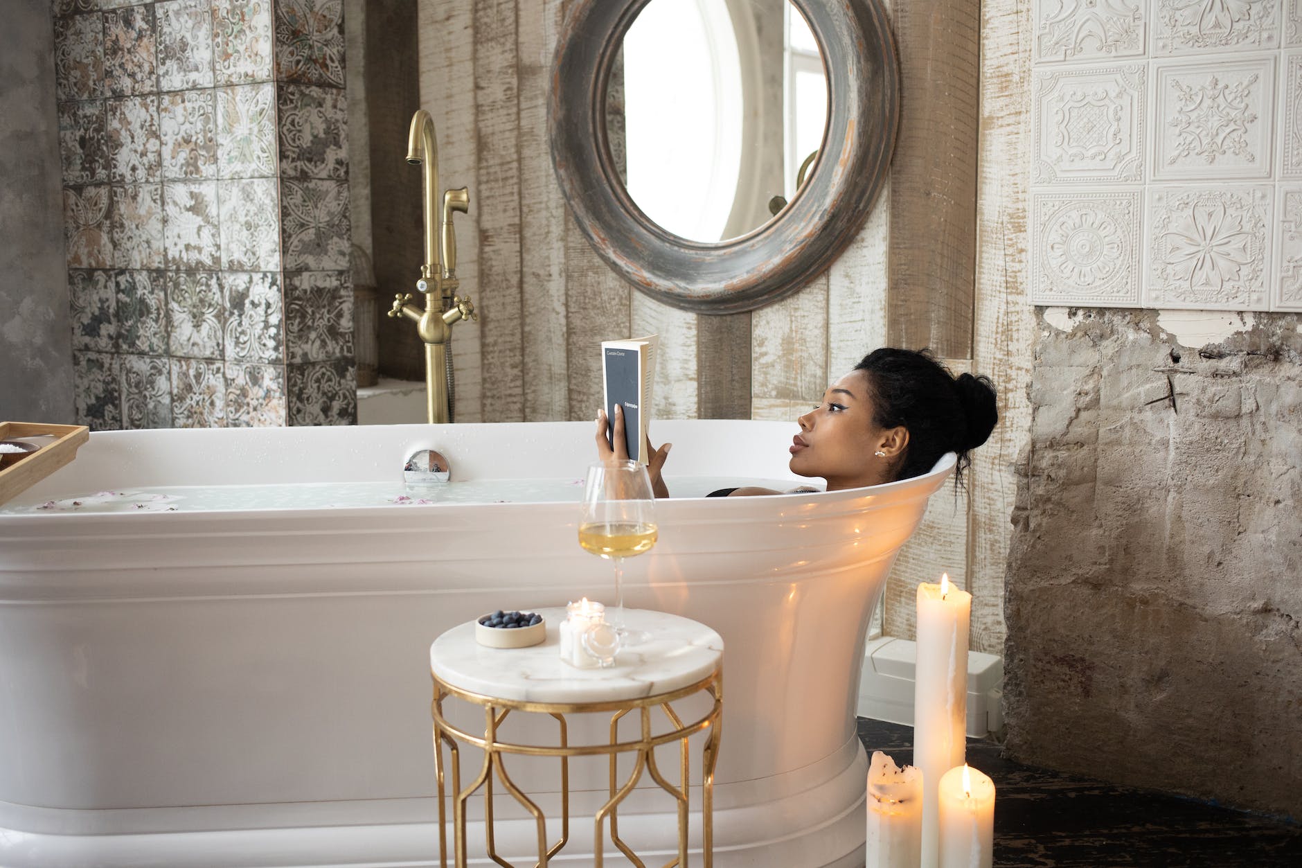 black woman reading book while taking bath with candles and champagne