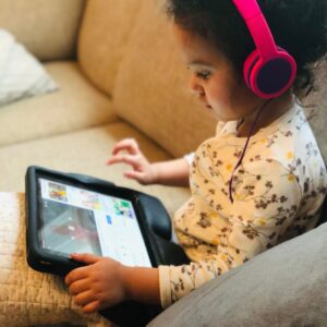 A little girl wearing headphones is engrossed in using an iPad while practicing digital parenting.