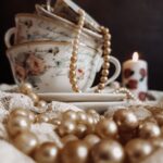 Stacked vintage teacups with floral patterns, accompanied by draped pearl necklaces and a right-time-to-declutter lit candle in a cozy, dimly-lit setting.