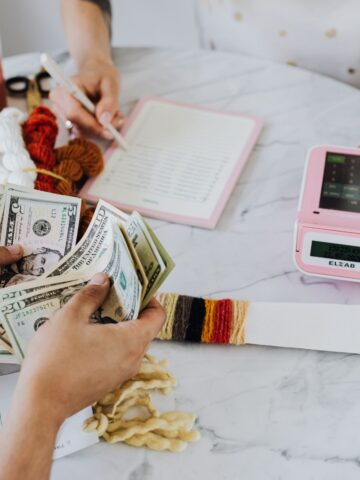 How to Plan Your Finances for the Whole Family Two people at a table with yarn and a digital scale, one holding cash and the other taking notes, in a craft project setup for extra income.