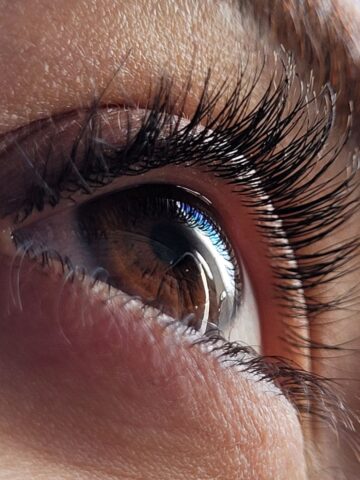 Close-up of a healthy vision human eye with detailed eyelashes and a visible reflection in the brown iris.