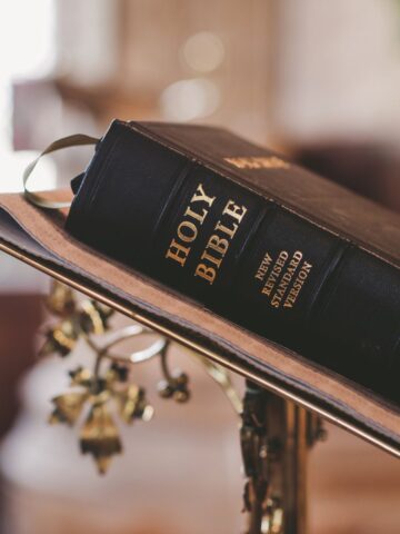 A holy bible placed on a wooden lectern with a golden cross visible in the background and "Secrets of the Bible" written on its cover.