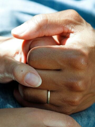 How to Support Loved Ones with Skin Cancer Close-up of interlocked hands with a visible wedding band, resting on a denim-clad lap, symbolizing skin cancer support.