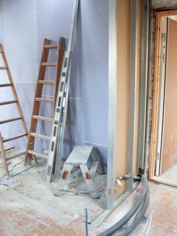 Interior construction site showing exposed walls, a ladder, electrical cables, and construction materials scattered around for a home renovation.