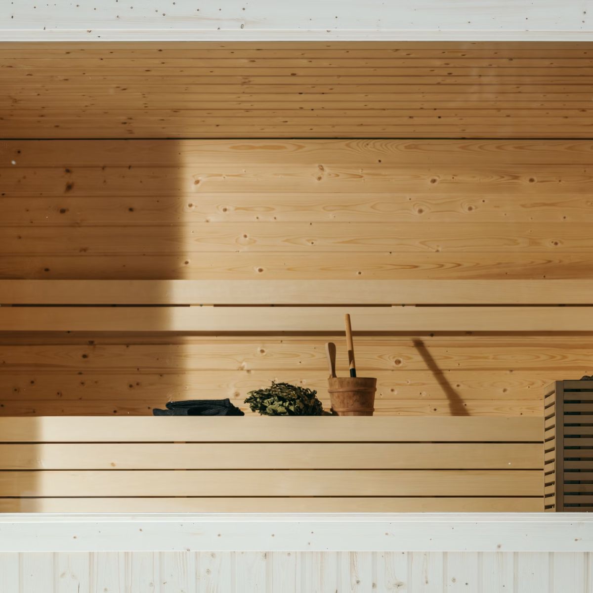 A wooden outdoor sauna interior with benches, a bucket, ladle, towels, and a bundle of twigs offers numerous health benefits.