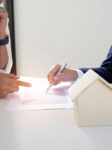 Two people discussing a mortgage application at a table with a small wooden house model beside them.