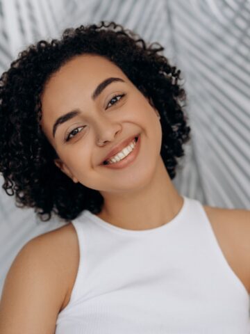 A person with short curly hair and a nose ring smiles while wearing a white tank top, envisioning a healthier future. A pattern of palm fronds is visible in the background.