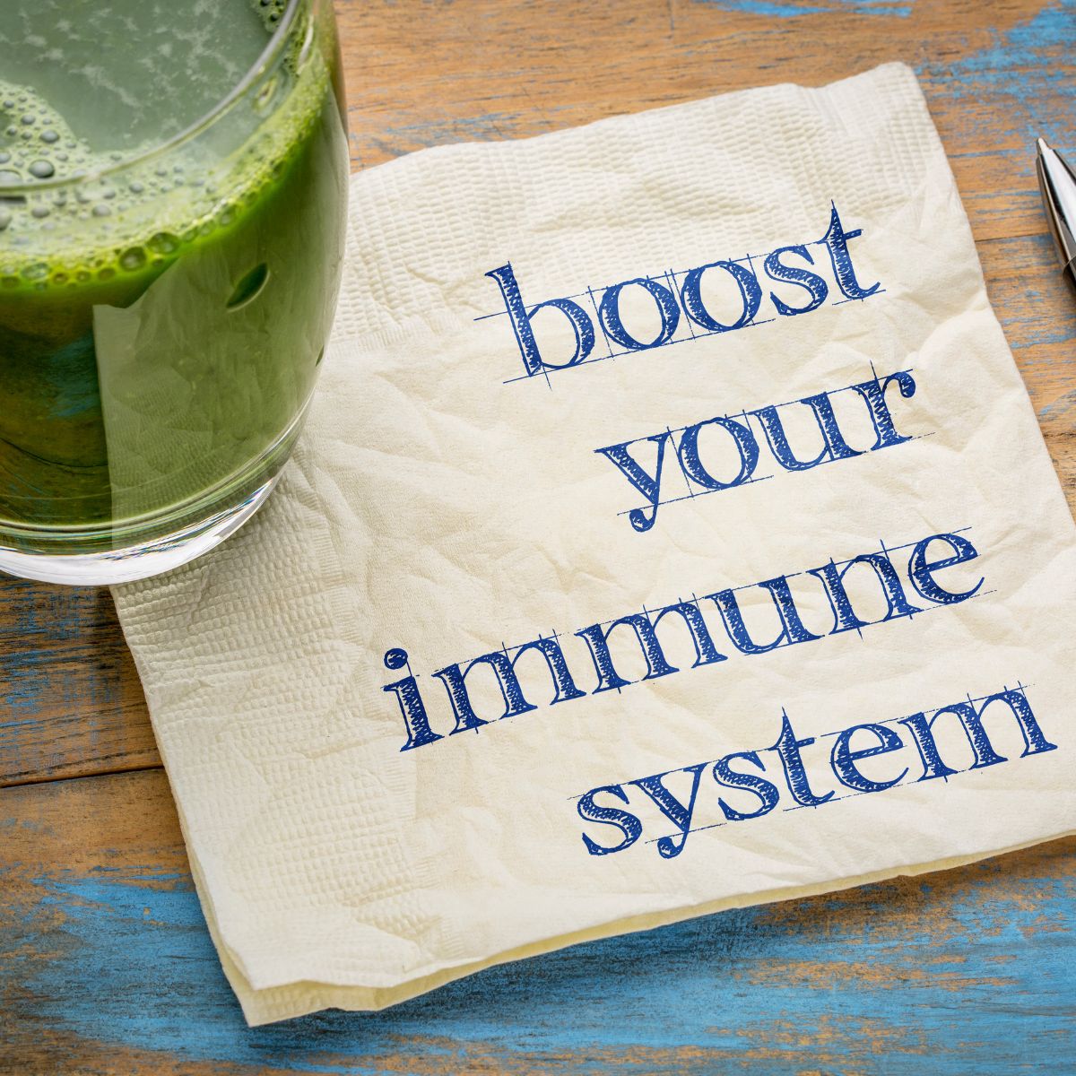 A glass of green juice sits next to a napkin with the text "Boost Immune System Tips" written on it.