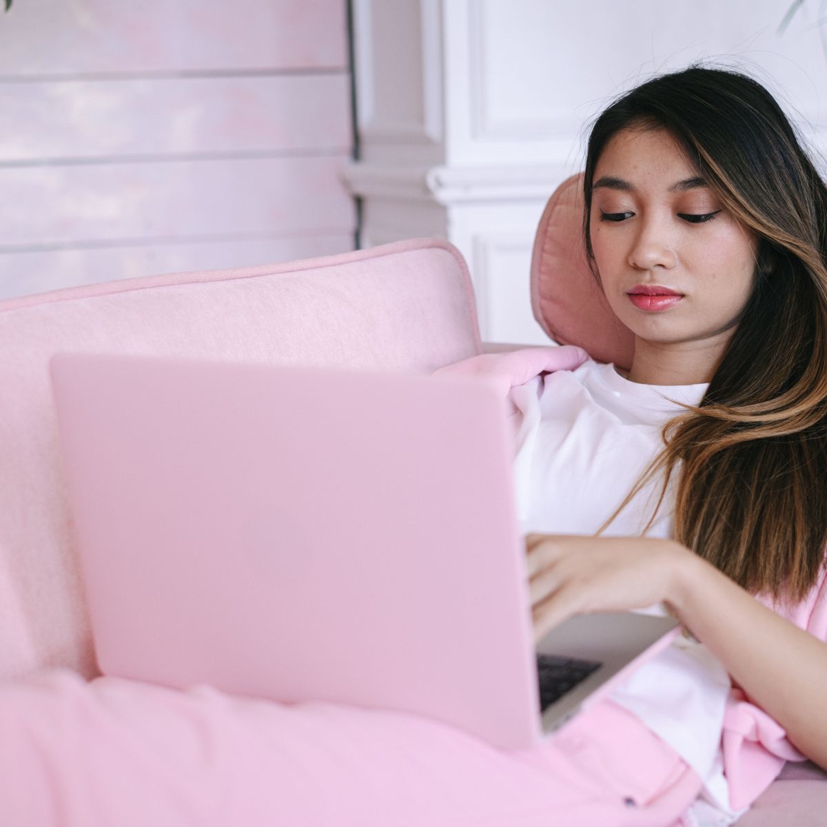 A person reclines on a sofa, using a laptop. They are wearing a white shirt and a pink jacket, matching the color of the reclining sofa. The scene exudes a sense of modern home comfort, hinting at how future living spaces blend style with relaxation.
