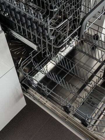 An open Bosch dishwasher with pull-out racks extended, positioned next to white cabinetry and a dark floor, showcases its long-lasting performance potential.