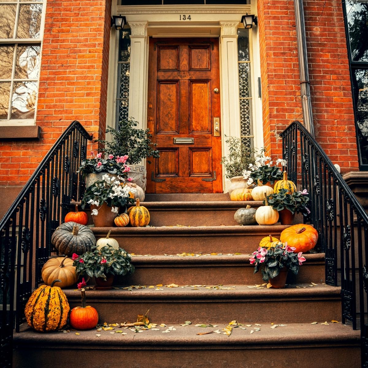 A brownstone front entrance with a wooden door, decorated with pumpkins and potted plants arranged along the steps, creates inviting autumn curb appeal—perfect for selling your home in a competitive market.