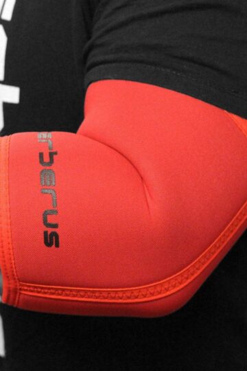 A person wearing a red elbow support sleeve with "Cerberus" text, perfect for weightlifting enthusiasts seeking optimal protection and performance.