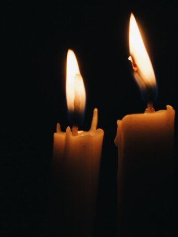 Two lit candles with melting wax against a dark background create a peaceful ambiance. If candle wax lands on clothes, consider exploring some handy tips for effective candle wax removal to keep your garments pristine.