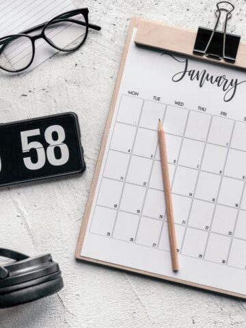 A January calendar on a clipboard with a pencil, black glasses, flip clock showing 9:58 AM, and headphones sits on a white textured surface-essential time management tools for ADHD adults looking to master deadlines.