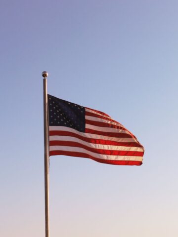 The U.S. flag waves on a flagpole against a clear blue sky.