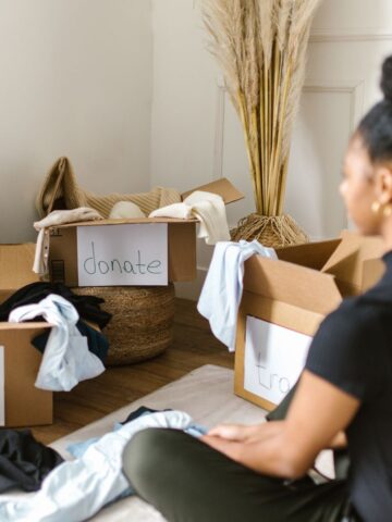 Decluttering for a Fresh Start in 2025 Amidst decorative pampas grass, a person sits in 2025, sorting through clothes into boxes labeled "keep," "donate," and "trash," embracing a fresh start with this decluttering journey.