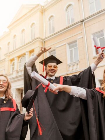 Graduates in caps and gowns celebrate a memorable moment, holding diplomas and smiling in front of a large building, as if the scene were the start of an unforgettable graduation party.