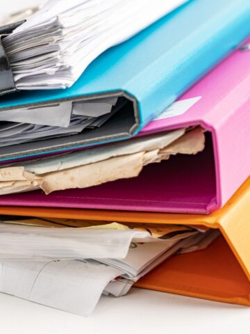 Stack of colorful binders filled with important paperwork, including blue, pink, and orange binders, ready to help organize bills at home on a white background.
