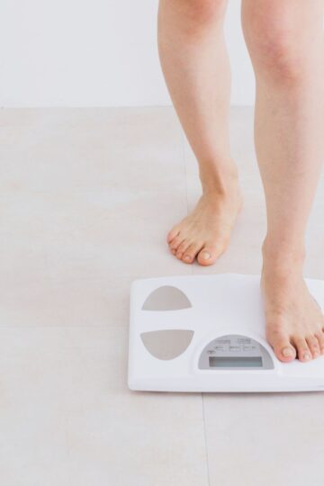 Person stepping onto a white digital scale on a tiled floor.