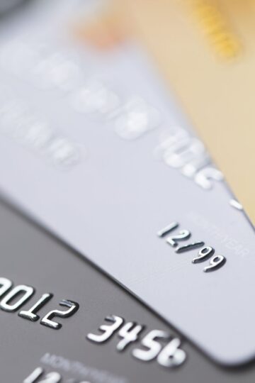 Close-up of three credit cards stacked, showcasing embossed numbers and expiration dates. Colors are silver, white, and gold. Gain insights into credit card cash advances as you explore the details captured in their elegant designs.