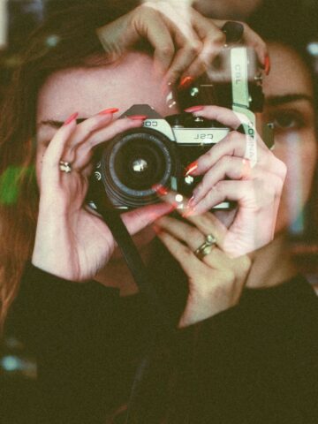 A person holds a camera up to their face. The double-exposed image, with overlapping hands and features, captures the creative essence of the best photography and highlights artistic experimentation within unique photography niches.