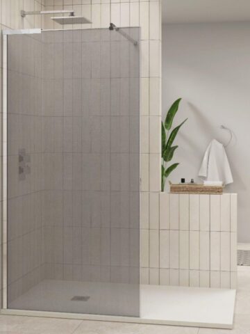 Modern bathroom in the UK featuring a sleek glass shower enclosure, beige-tiled walls, a towel hanging on a hook, a potted plant, and a basket on a ledge.