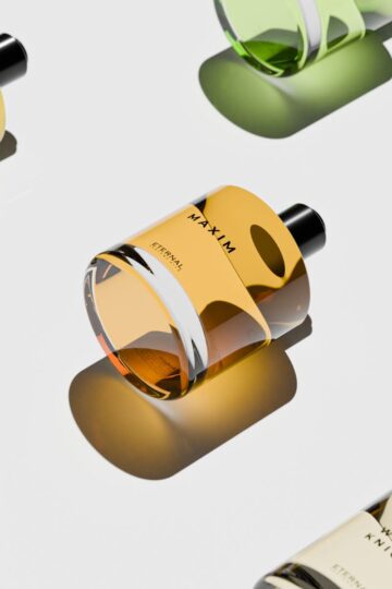 Four women's perfumes with black caps are arranged diagonally on a light surface. Bottles in green and amber exude an air of sensibility, with shadows elegantly cast below them, hinting at the exquisite scent each contains.