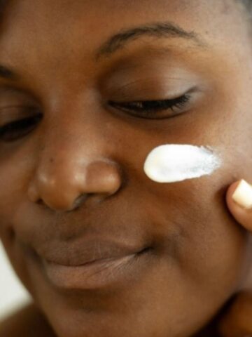 Person applying a dab of cream to their cheek with one finger, eyes closed, looking content as if they've discovered their new favourite product. It's part of a haul where everything's under £50, offering luxury without breaking the bank.
