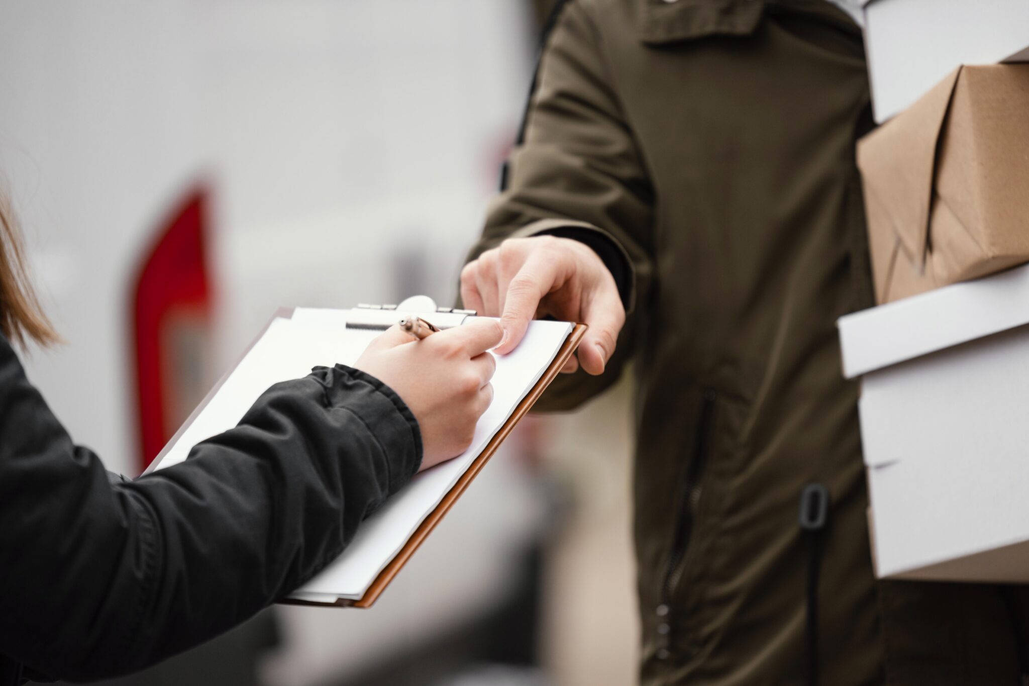 A person signs a clipboard held by another individual carrying cardboard boxes, likely confirming receipt of a delivery from a shop Kratom order, possibly featuring the best Kratom strain or MIT45 Kratom products.