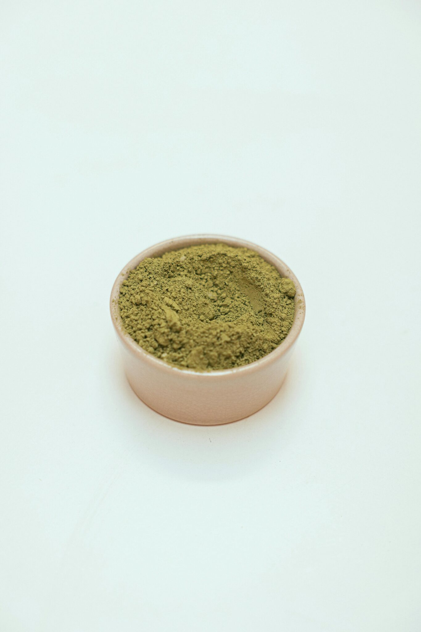 A small, round container filled with green powder sits on a plain white surface.