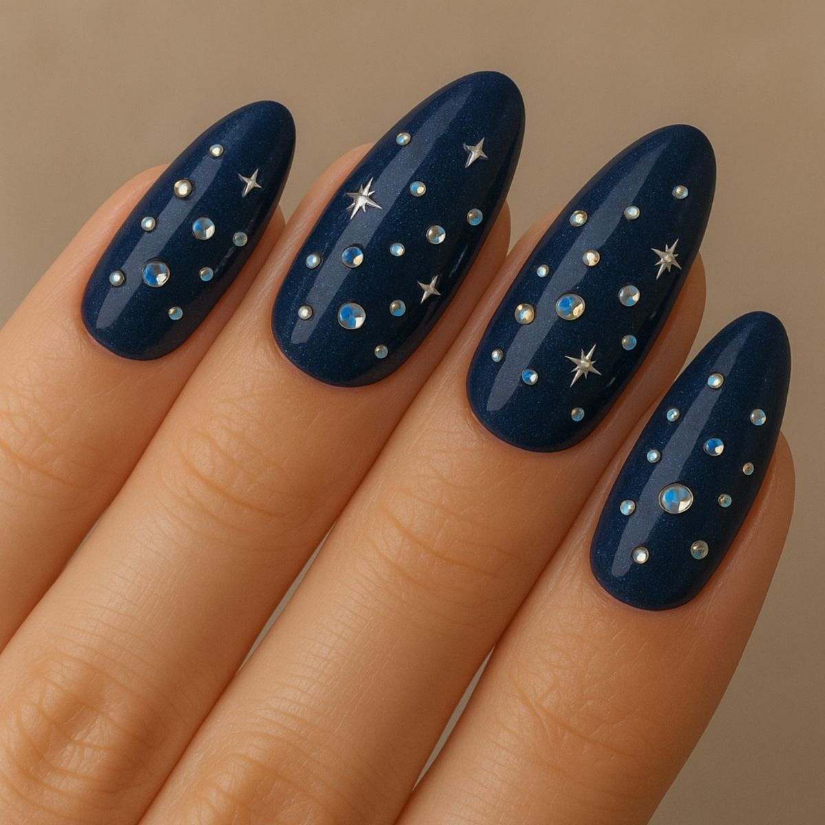 A hand with long, almond-shaped nails painted dark blue, decorated with small silver studs and star-shaped accents in a celestial pattern—perfect inspiration for those who love elegant Swarovski Nail Designs.