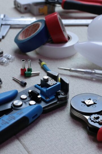 A variety of electrical tools and supplies—like pliers, screwdrivers, insulation tape, light bulbs, and connectors—often sourced from local electrical wholesalers or contractors, are neatly arranged on a light surface.